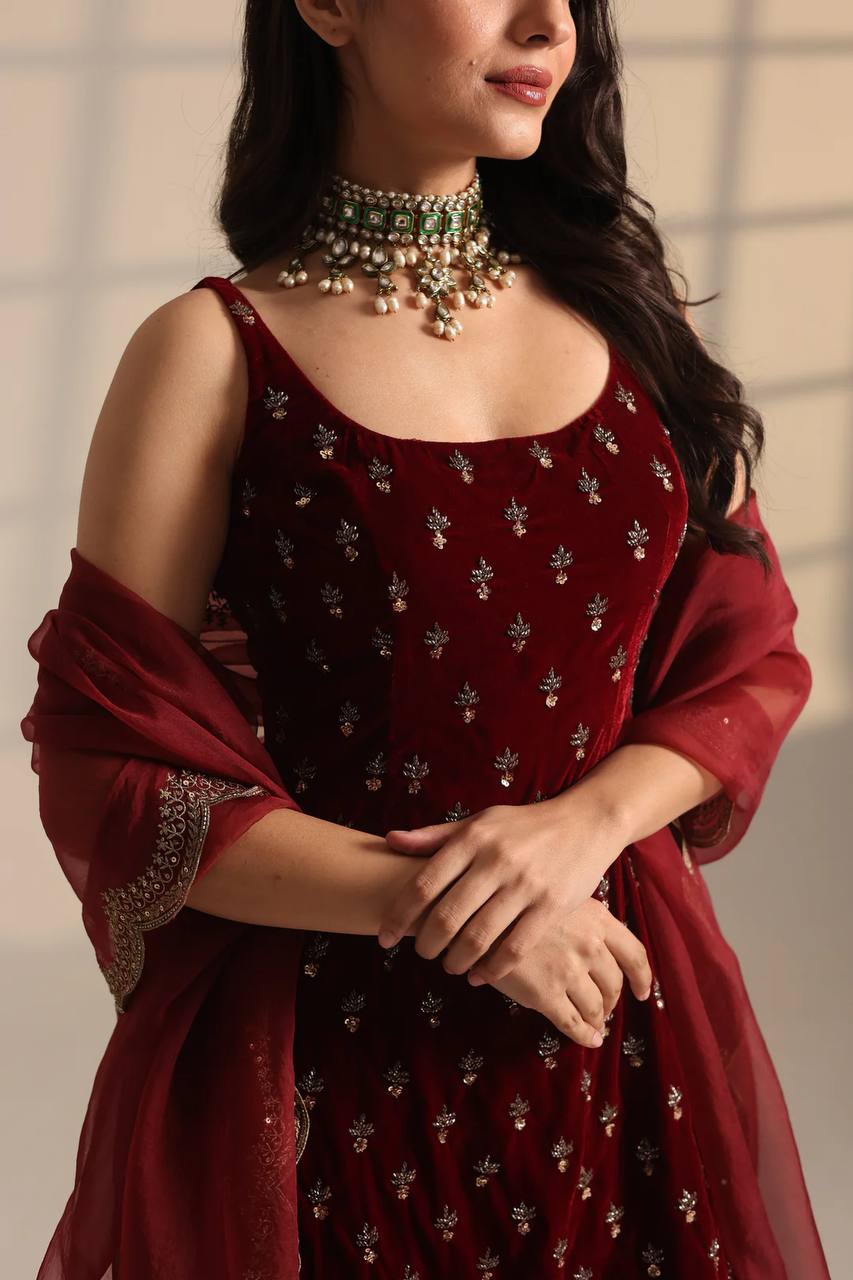 Woman wearing a maroon embroidered dress with a matching shawl against a neutral background