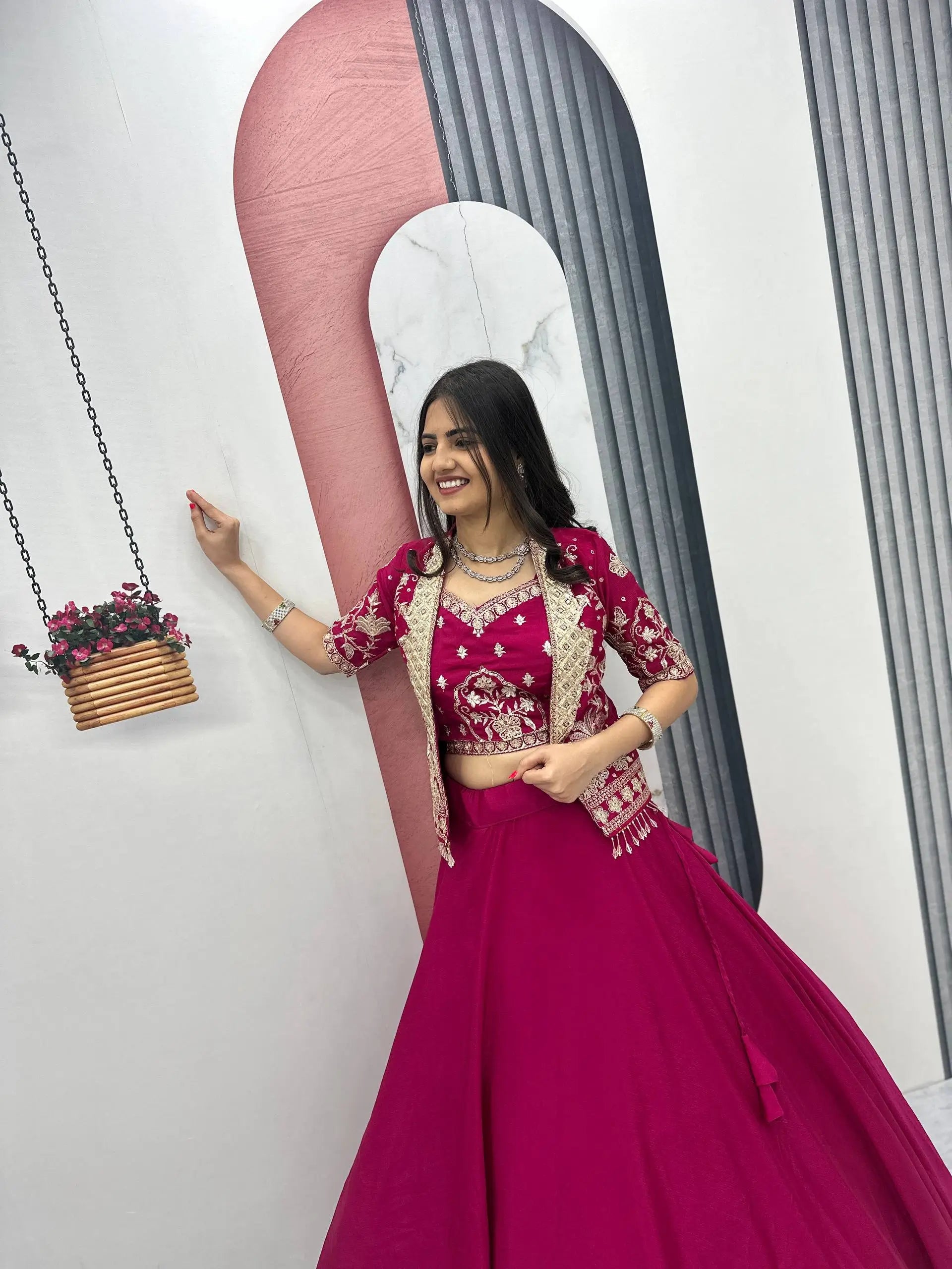 Woman in a pink traditional outfit posing in front of a decorative wall with a pink and gray abstract design.