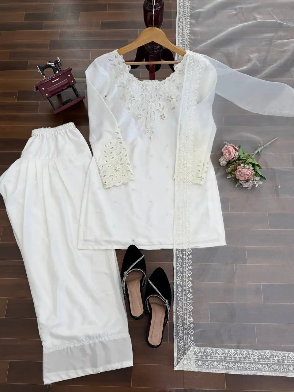 White embroidered outfit with pants and a dupatta on a wooden floor.
