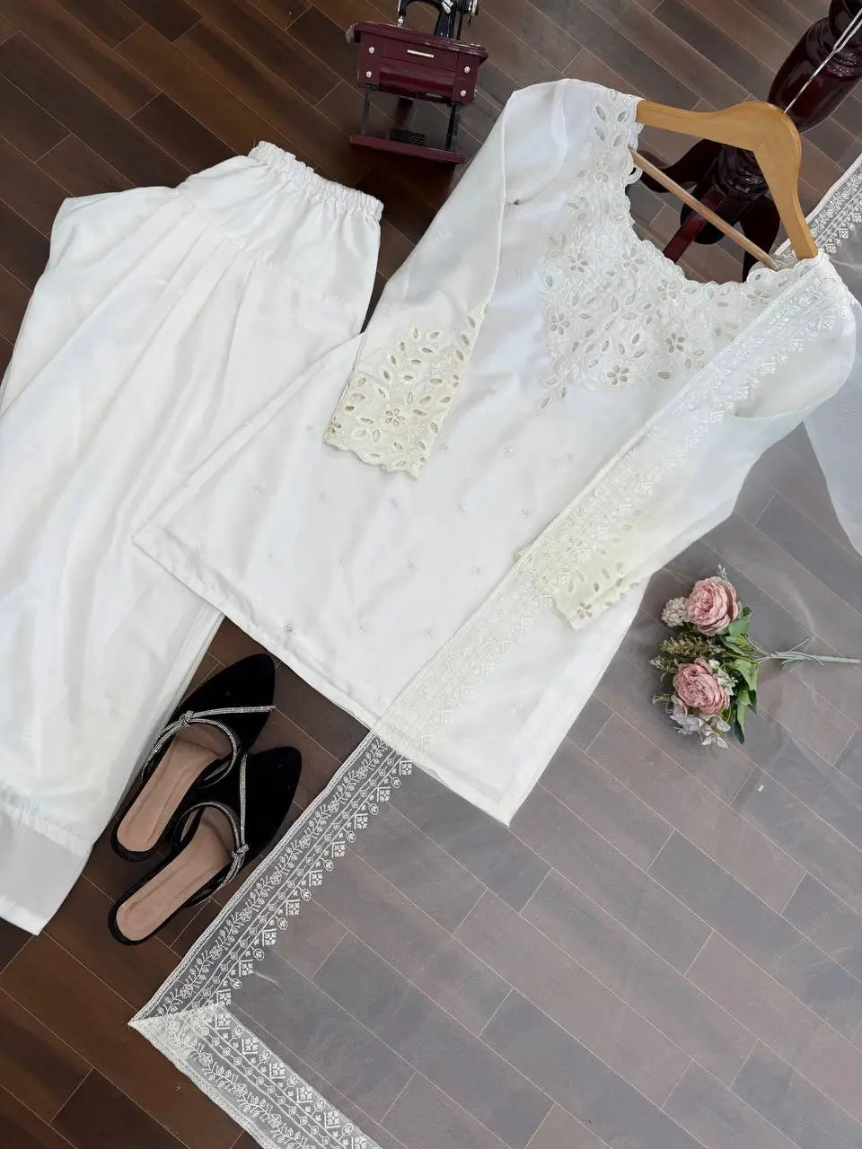 White lace top and pants on a wooden floor with a small table and shoes in the background.