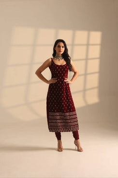 Woman wearing a maroon traditional outfit with a patterned dress against a beige wall.