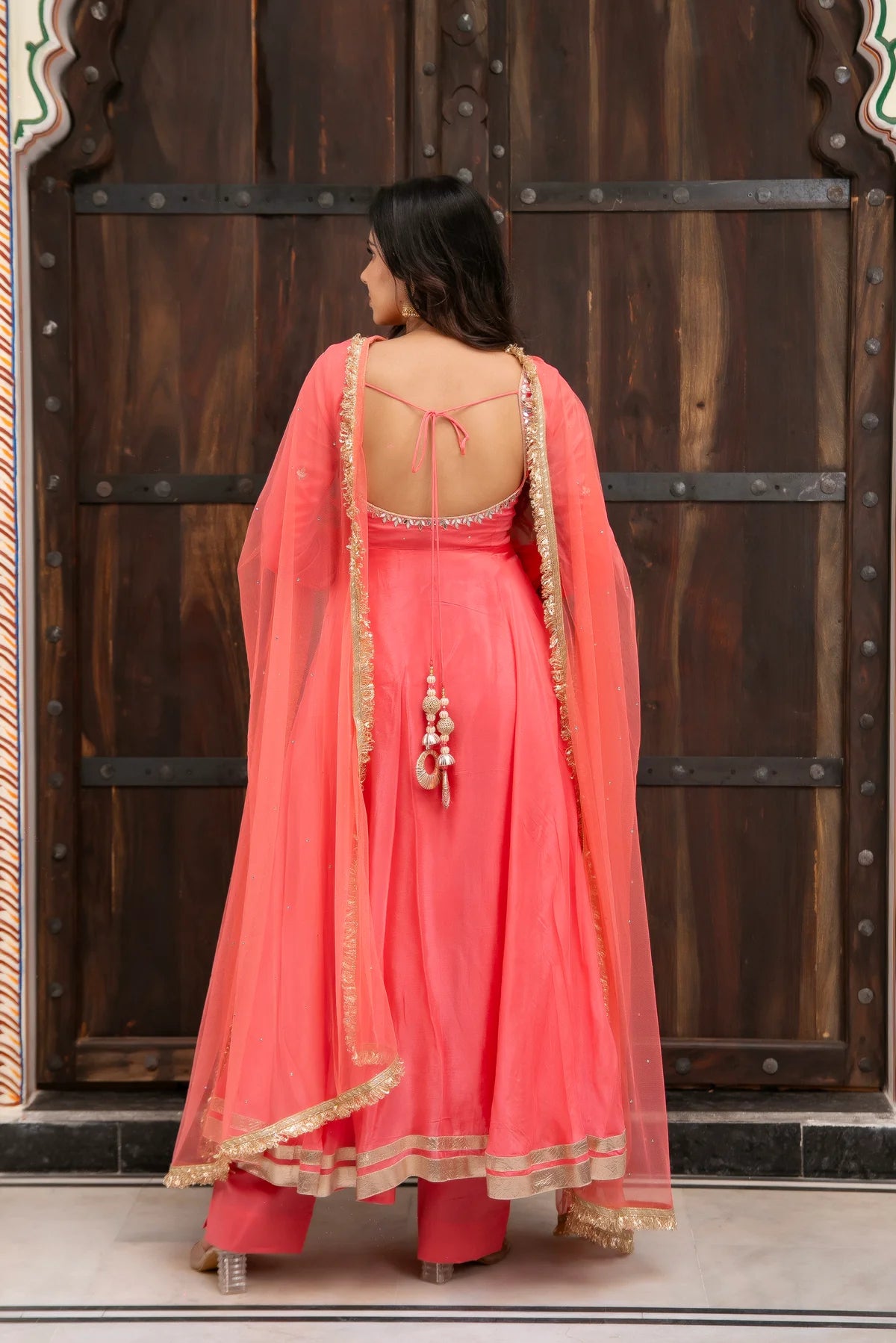 back view of coral pink anarkali with open tie design and gold net dupatta