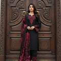 Woman in black and red traditional outfit standing in front of a wooden door with intricate carvings.
