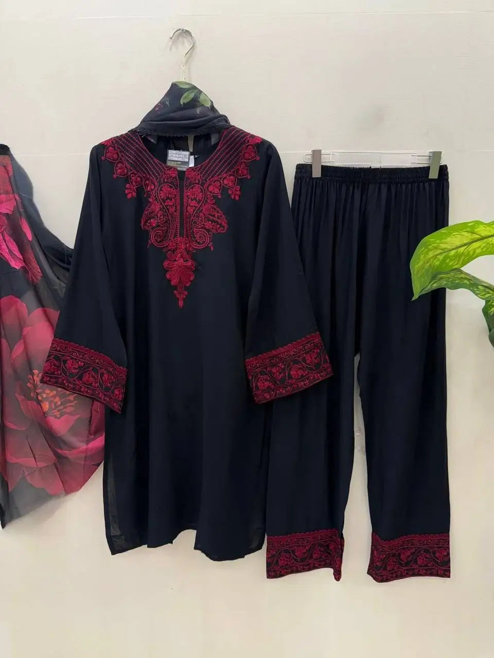 Black outfit with red embroidery on a hanger against a white background