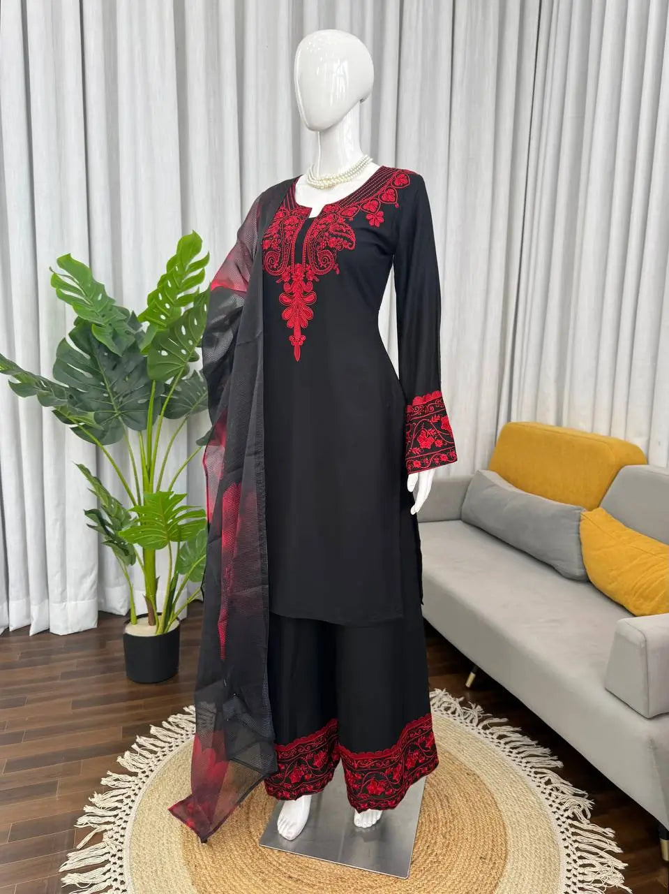 Black outfit with red embroidery on a mannequin in a room with a sofa and plant.