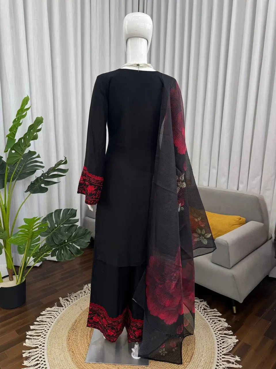 Mannequin wearing a black outfit with red floral patterns in a room setting.