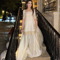 Woman in a white and gold traditional outfit standing on a staircase at night.