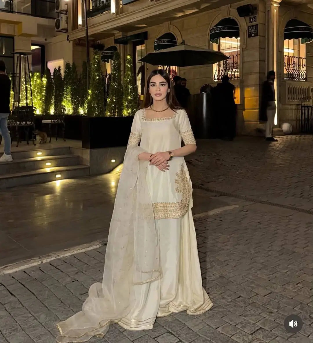 Woman in a traditional outfit standing on a street at night.