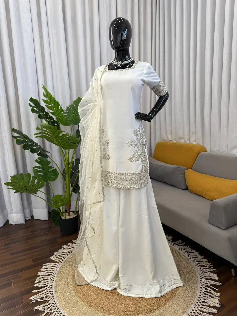 White saree with intricate patterns on a mannequin in a living room setting.