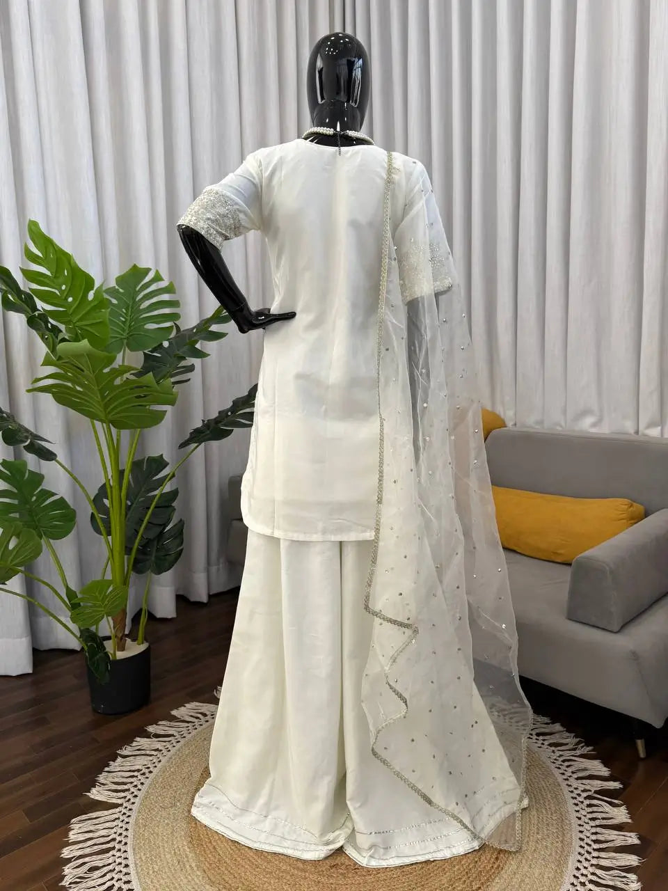 White traditional outfit on a mannequin against a neutral background with plants and furniture.