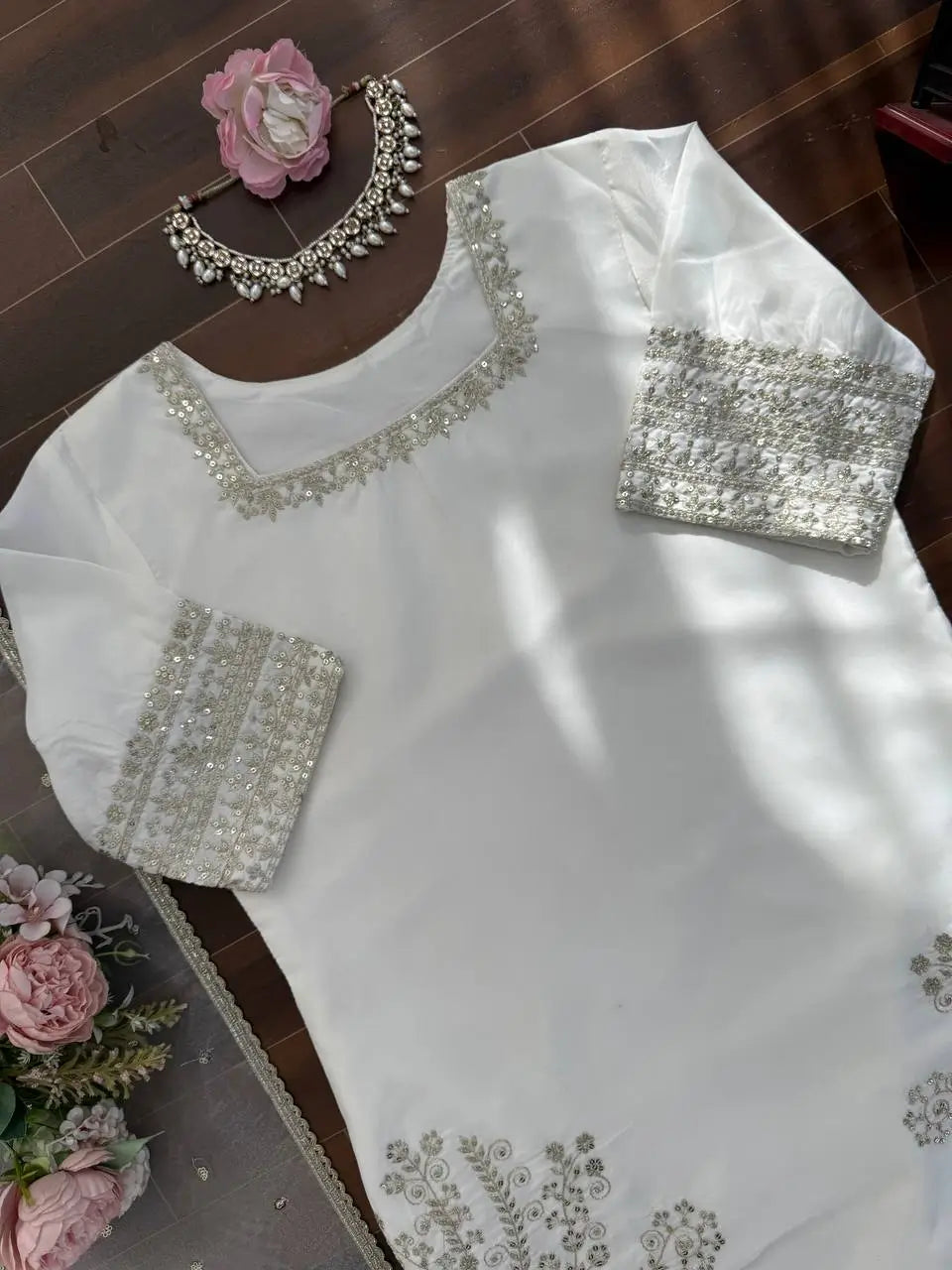 White embroidered blouse with silver details on a wooden surface with flowers and jewelry.