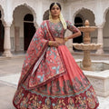Woman in traditional pink and red embroidered outfit standing in a courtyard with arches and a fountain.