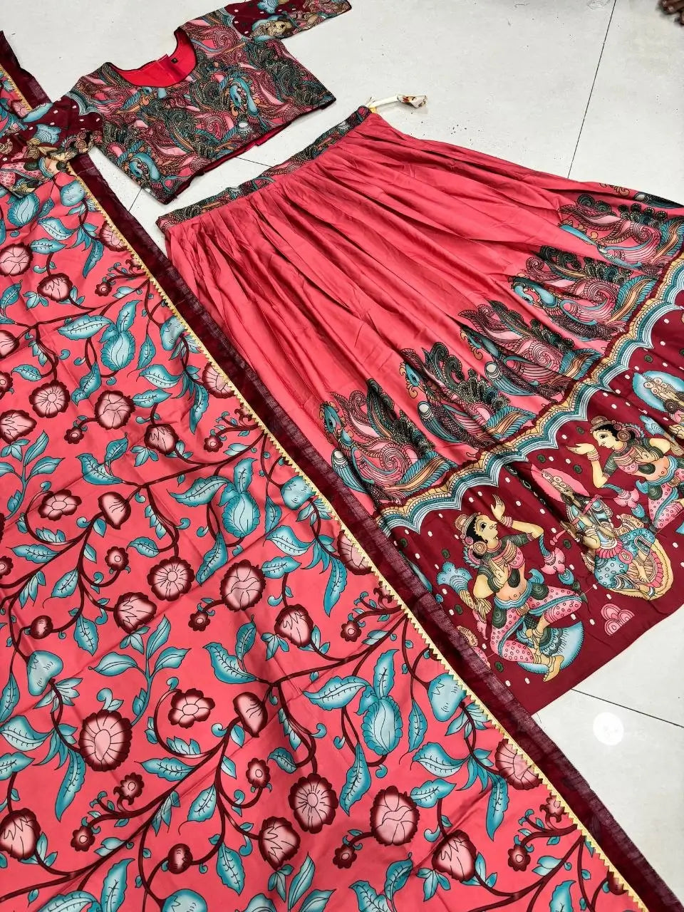 Red traditional outfit with floral and deity designs on a tiled floor