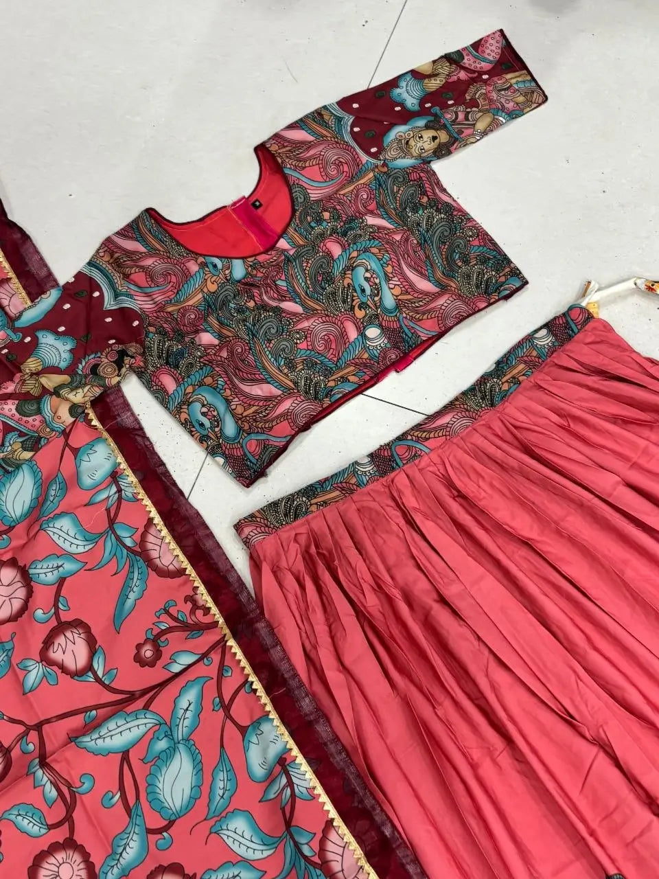 Traditional outfit with a patterned blouse and red skirt on a white floor.