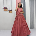 Woman in a pink traditional outfit standing in a minimalistic room with plants.