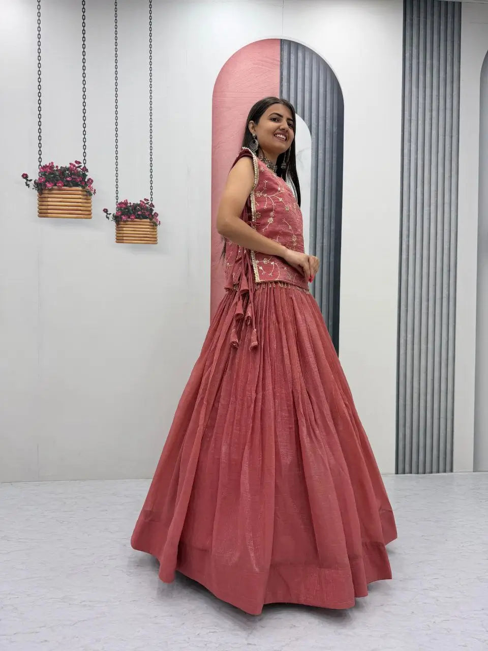 Woman in a pink dress standing in a room with a mirror and plants.