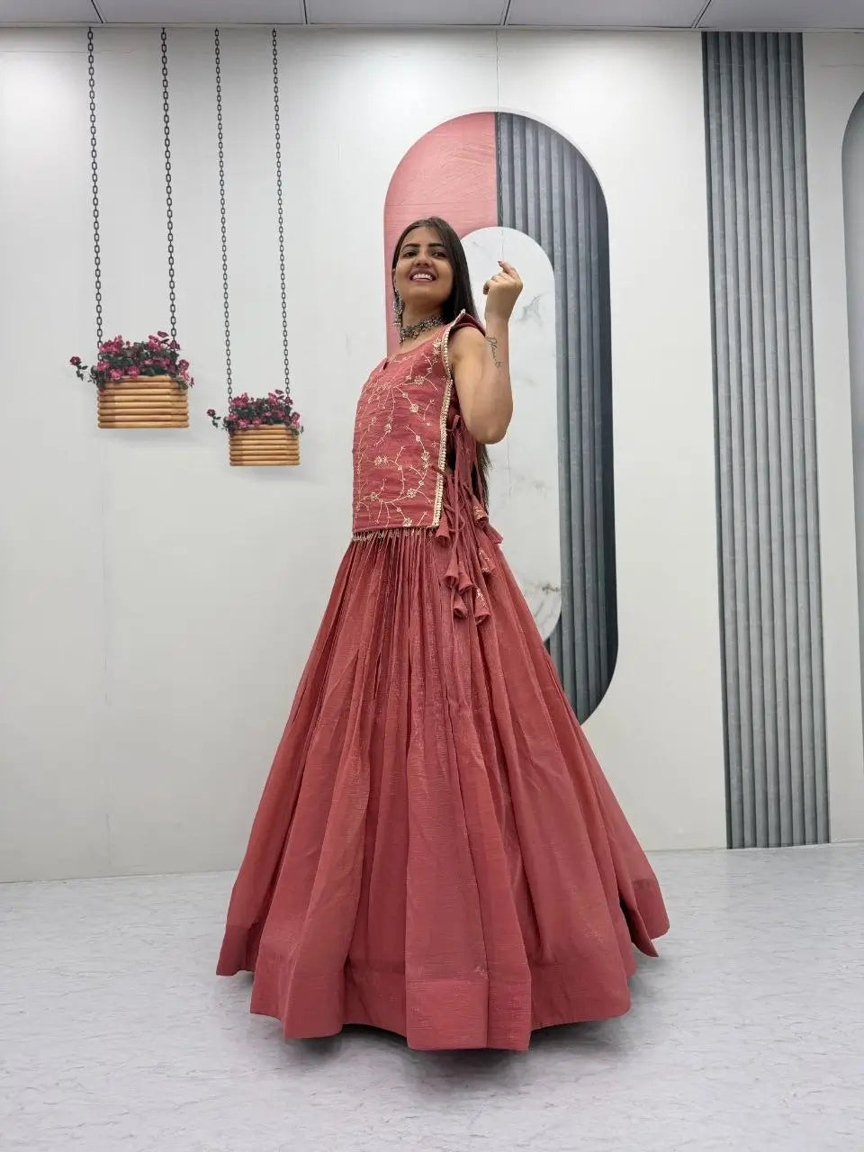 Woman in a pink traditional outfit standing in front of a mirror with decorative plants on the wall.