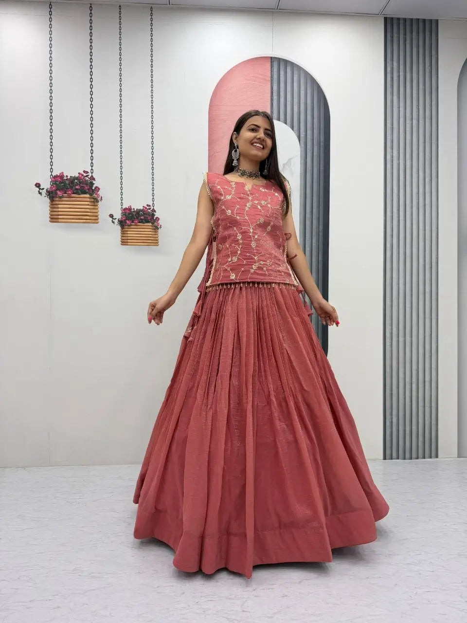 Woman wearing a pink traditional outfit with a long skirt in a minimalistic room.
