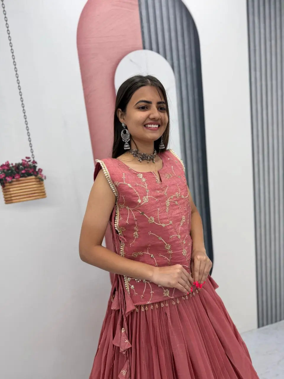 Woman in a pink traditional outfit standing indoors with a decorative background.