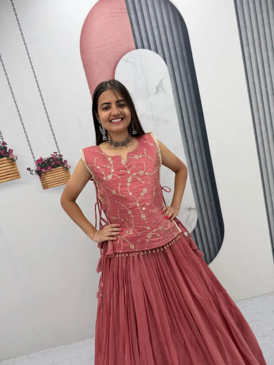 Woman in a pink traditional outfit standing in a minimalistic room with decorative elements.