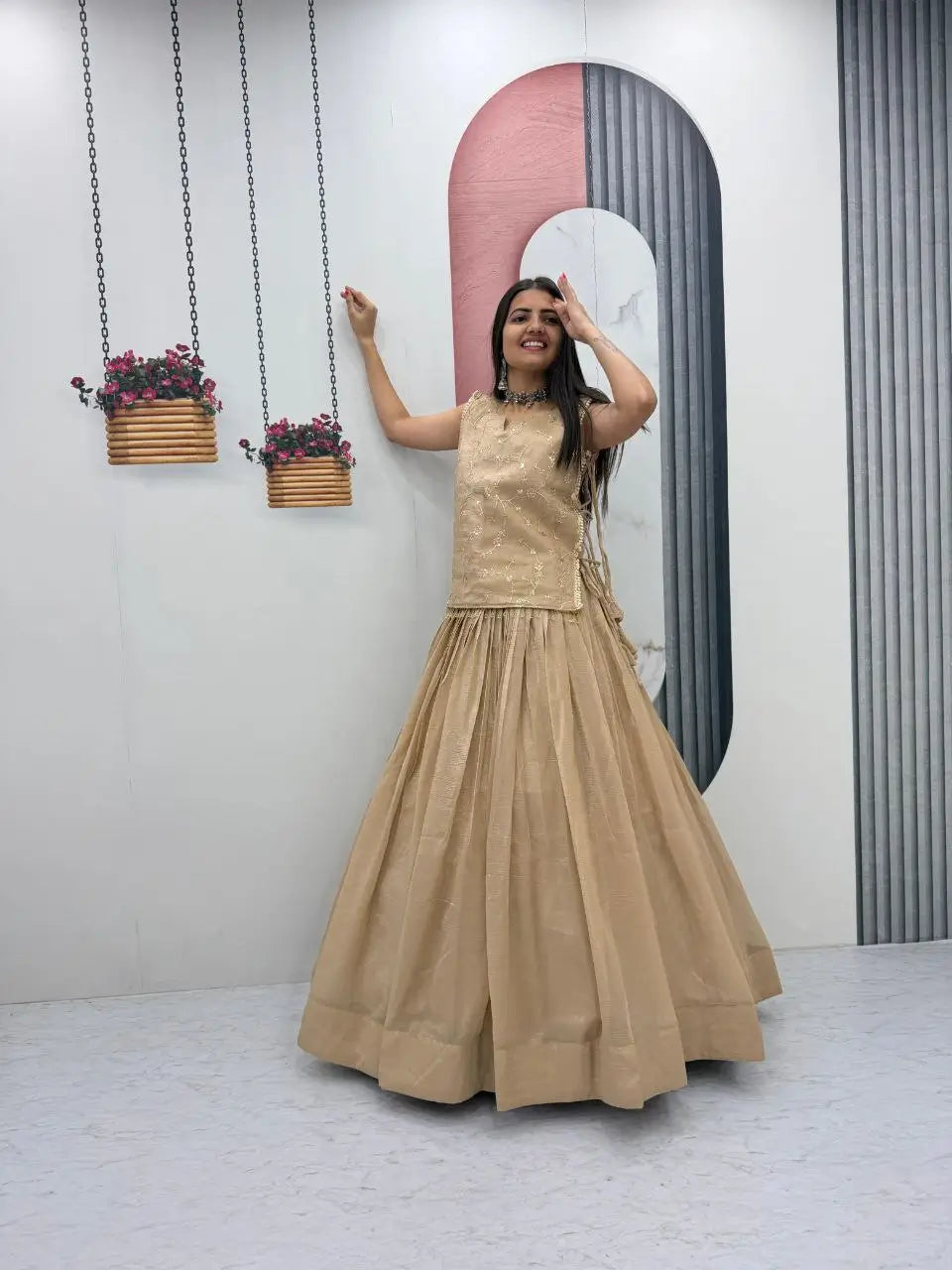 Woman in a beige dress standing in front of a decorative wall with hanging plants.