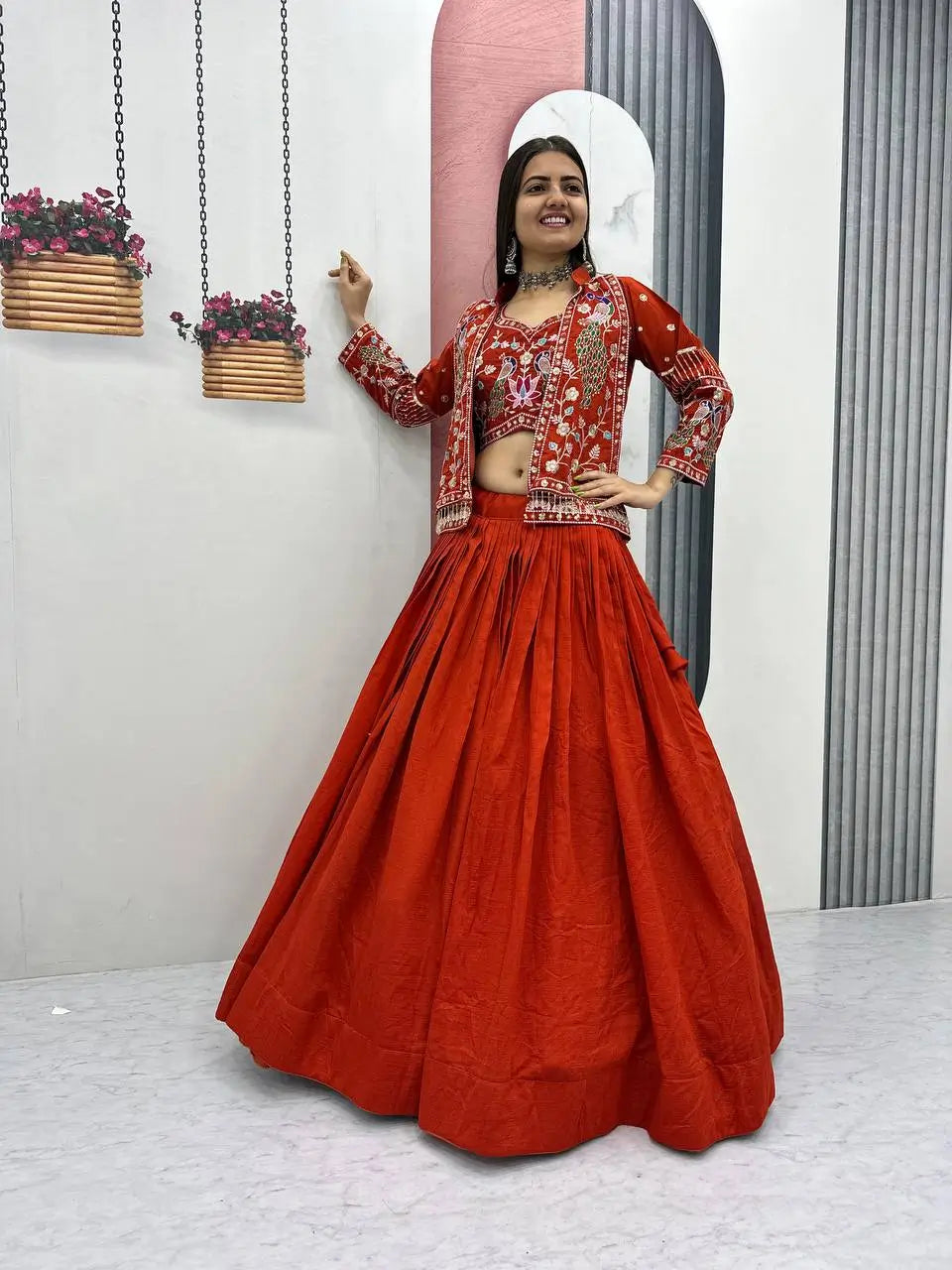 Woman in a red traditional outfit with floral patterns standing in a minimalistic room.