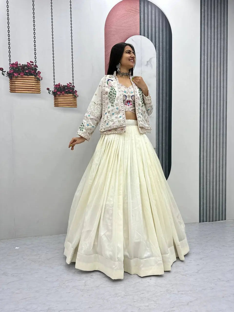 Woman in a white traditional outfit standing in a minimalistic room with plants hanging from the ceiling.
