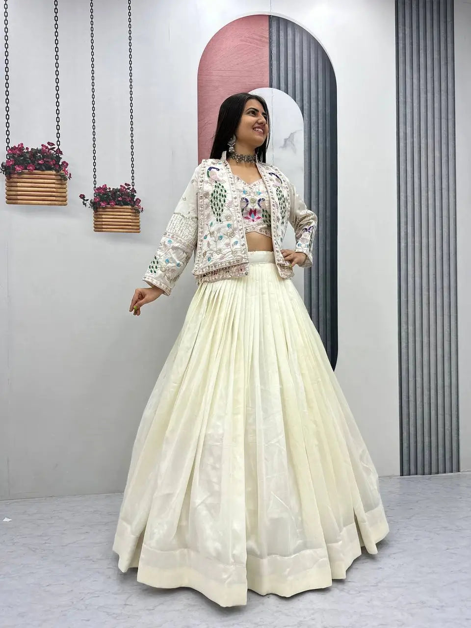 Woman in a cream traditional outfit with floral patterns in a minimalistic setting.