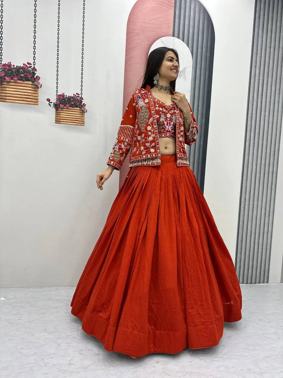 Woman wearing a red traditional outfit with a matching skirt in a minimalistic setting.