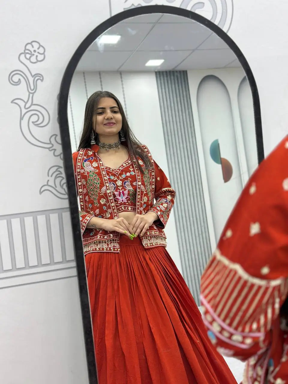 Woman in a red traditional outfit standing in front of a mirror.