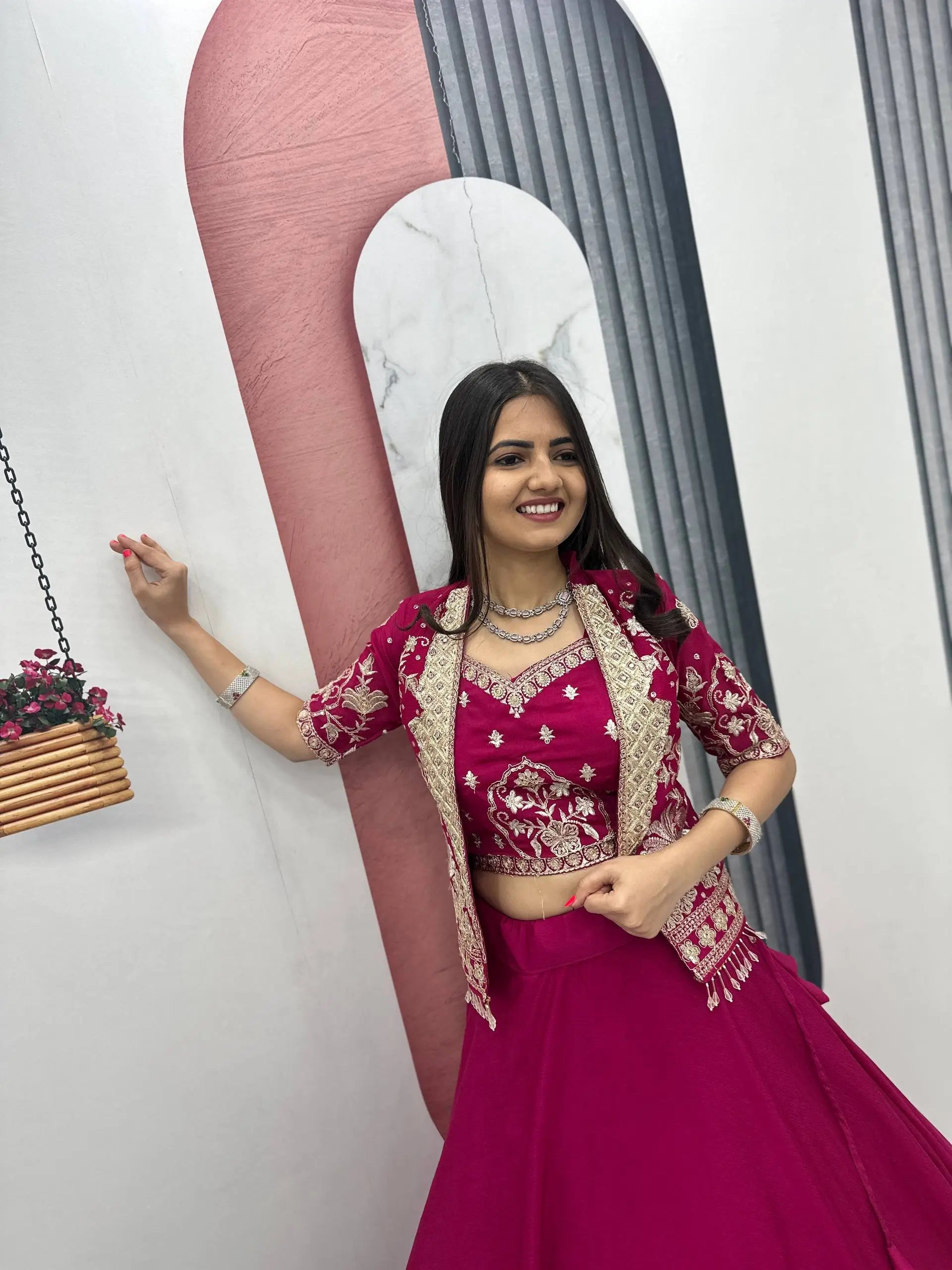 Woman in a pink traditional outfit posing indoors with decorative elements.