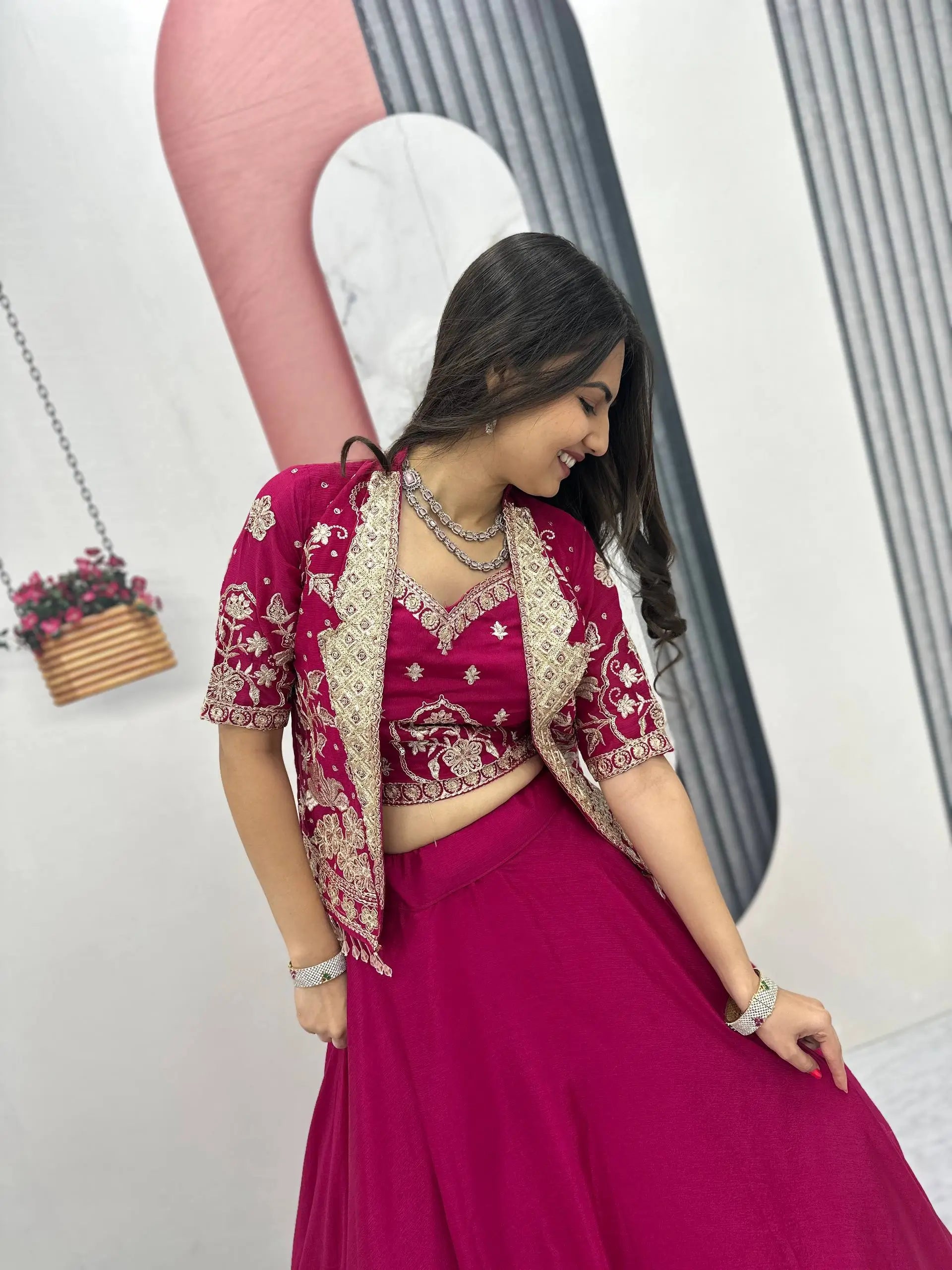 Woman in a pink traditional outfit with gold embroidery, standing indoors.