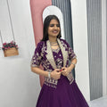 Woman in a purple traditional outfit standing in front of a decorative archway.
