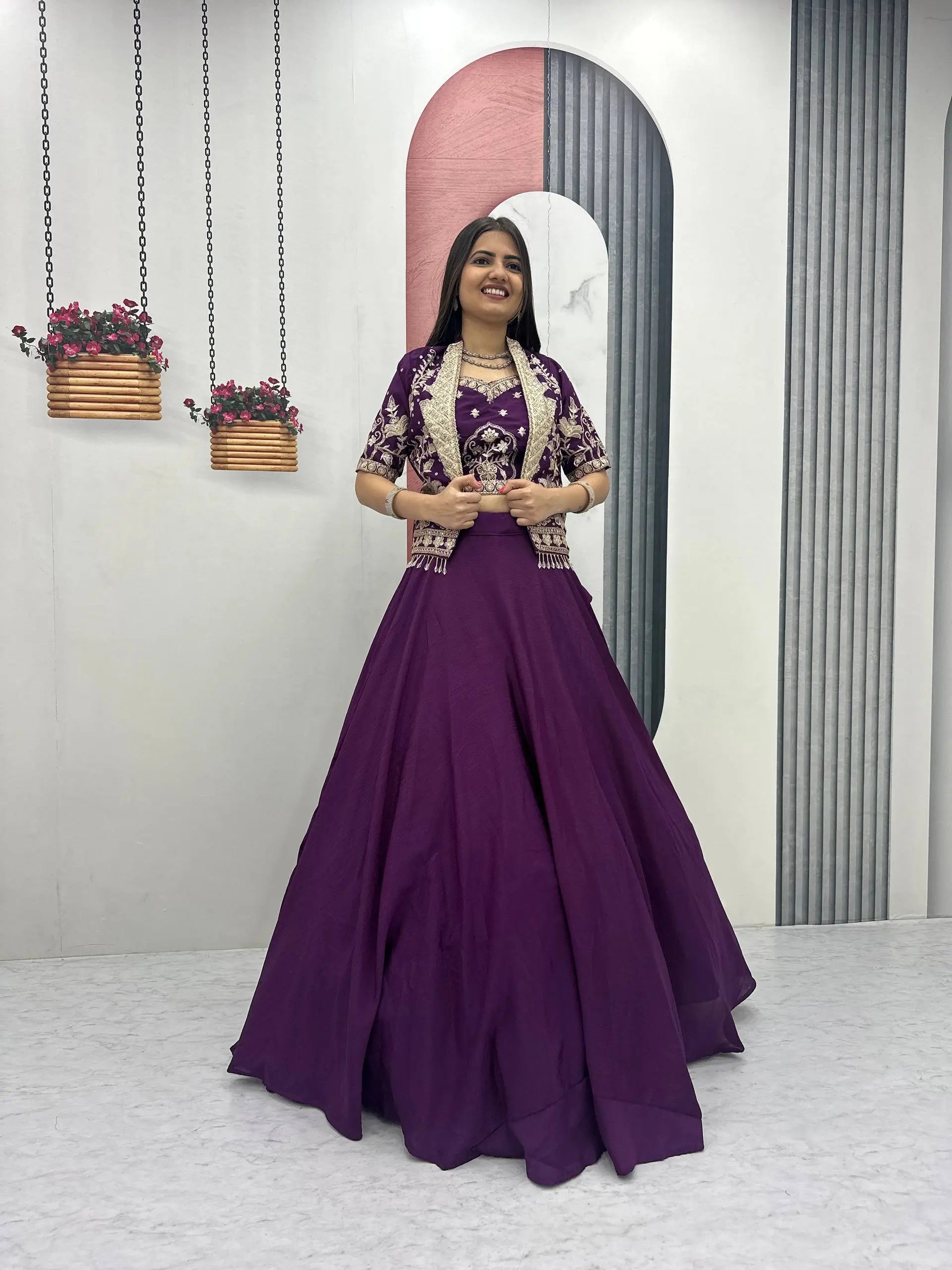 Woman in a purple traditional outfit standing in a minimalistic room with plants and a mirror.