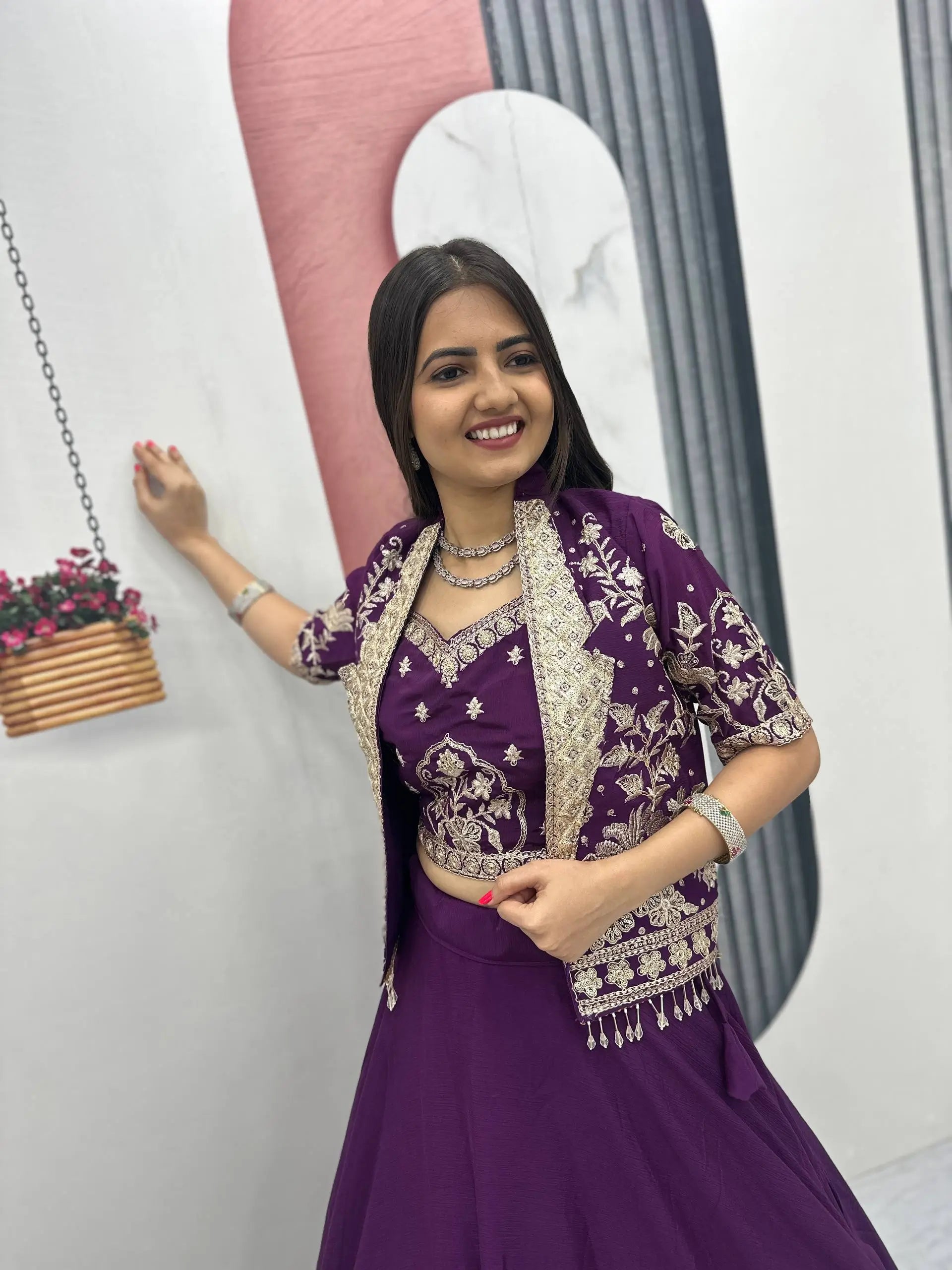 Woman in a purple traditional outfit with gold patterns standing indoors.