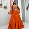 Woman wearing an orange traditional outfit with a matching dupatta in a minimalistic room.
