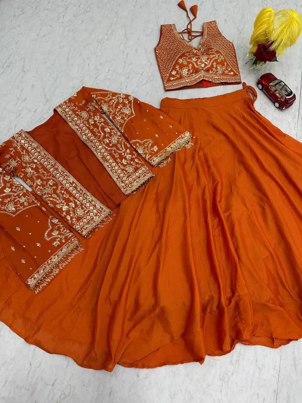 Orange traditional outfit with intricate patterns on a light gray surface.