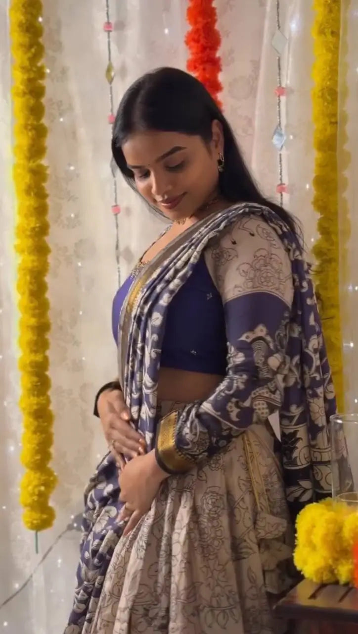 Woman in traditional attire standing against a decorated background with flowers and lights.