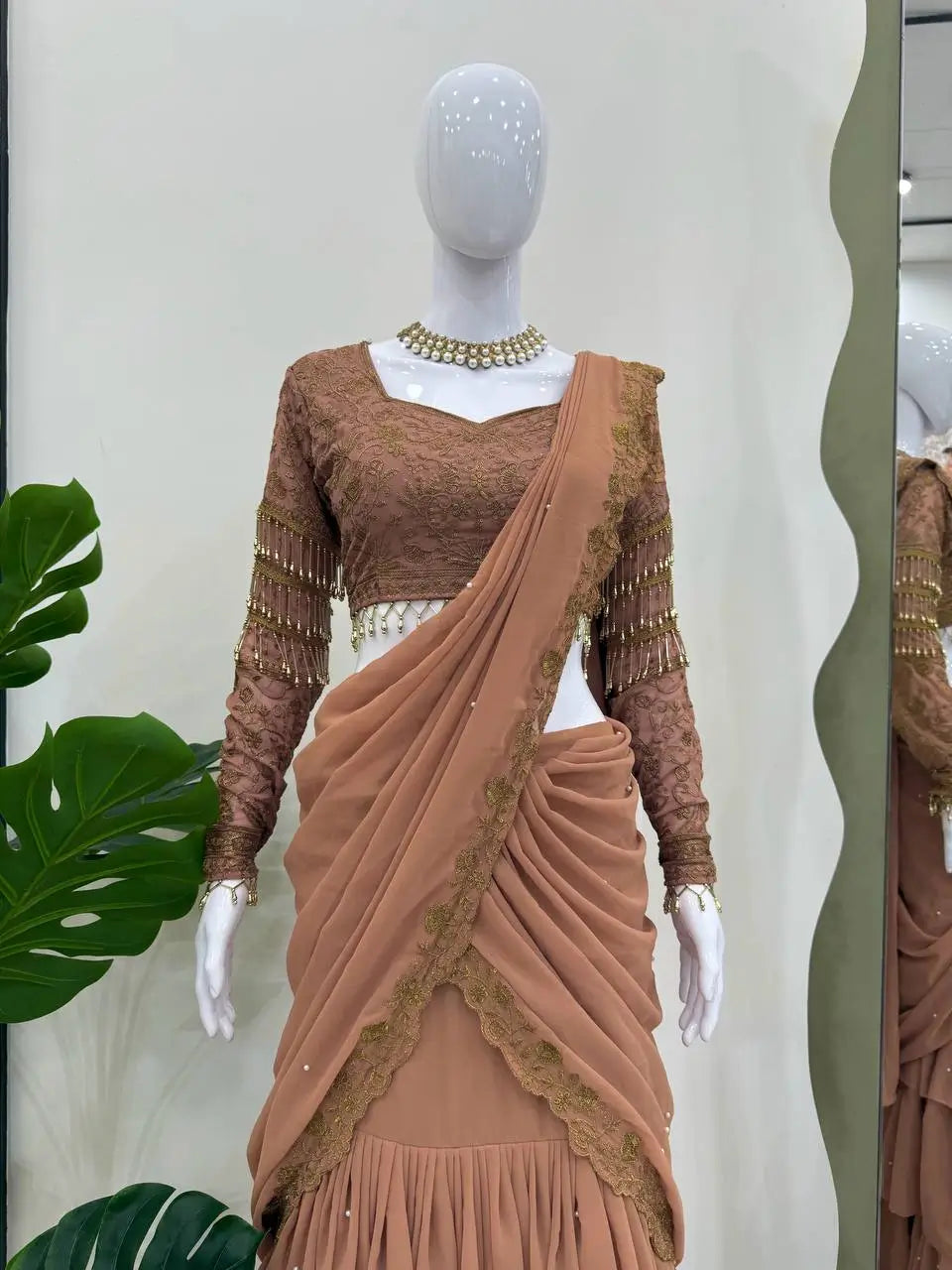 Elegant brown ethnic saree with gold embroidery, lace blouse, and pleated skirt, styled on mannequin with pearl necklace